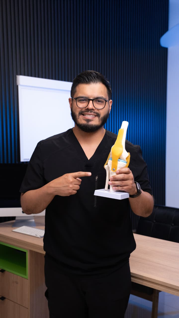 Dr. Luis Eduardo Flores explicando un modelo anatómico de rodilla en consulta